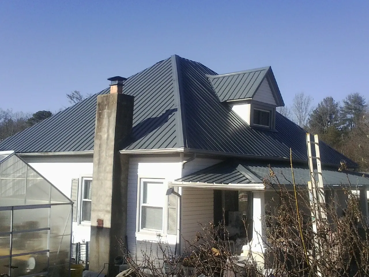 Dark blue standing seam metal roof on a white farmhouse with dormer — Slate & Tile Roof Repair by Roofing Brothers in Peak