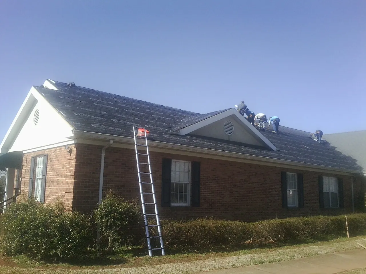Crew tearing shingles off a brick ranch roof with a ladder set — Metal Roof Repair work by our crew in Peak