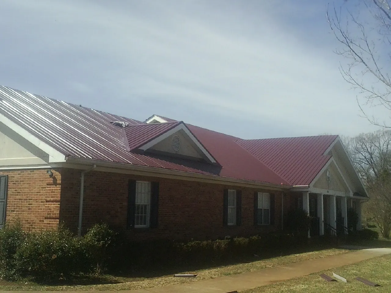 Red metal roof with gabled entries on a long brick building, from a Hail Damage Roof Repair job in Peak
