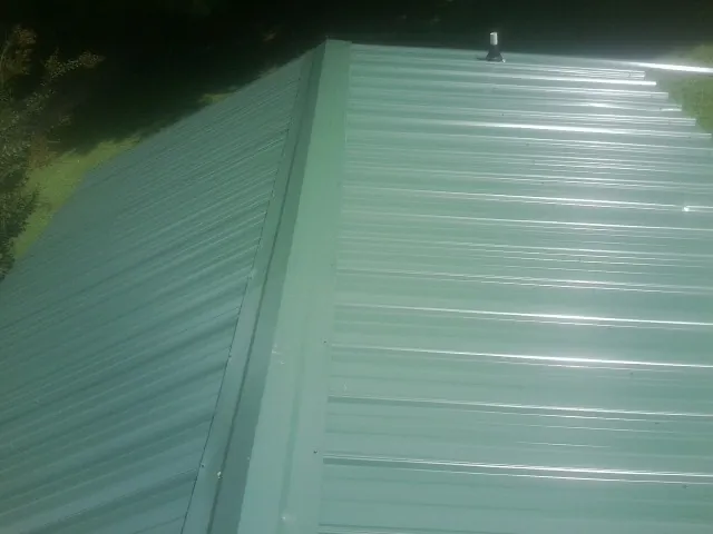 New green metal panels meeting at the ridge of a roof — Flat Roof Repair work by our crew in Peak