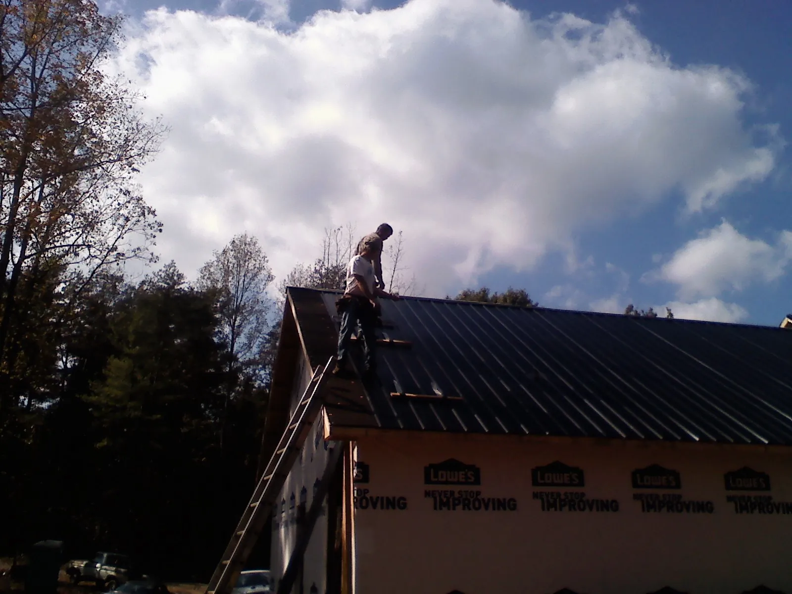 Roofer fastening dark metal panels high against a cloudy sky, from a Roof Inspection job in Peak