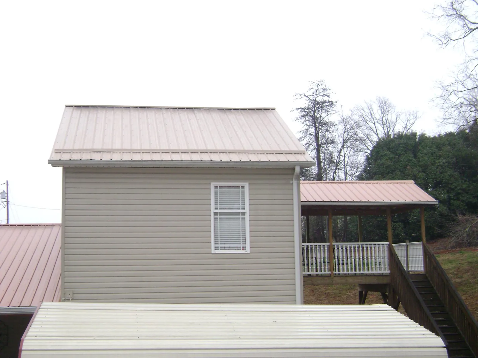 Tan metal roofs on a two story addition and attached porch, from a Roof Replacement job in Peak